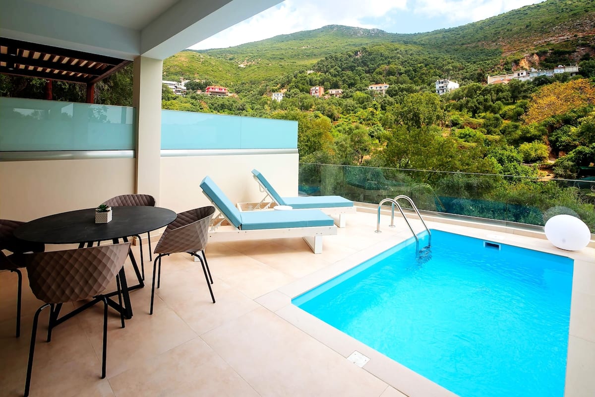 A balcony with a pool, lounge chairs, and a table with chairs.
