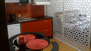 A compact kitchen with a microwave, coffee maker, and a sink. There is a red cabinet and a decorative partition with a geometric pattern. - Metro-Apartment - Porto (Porto)