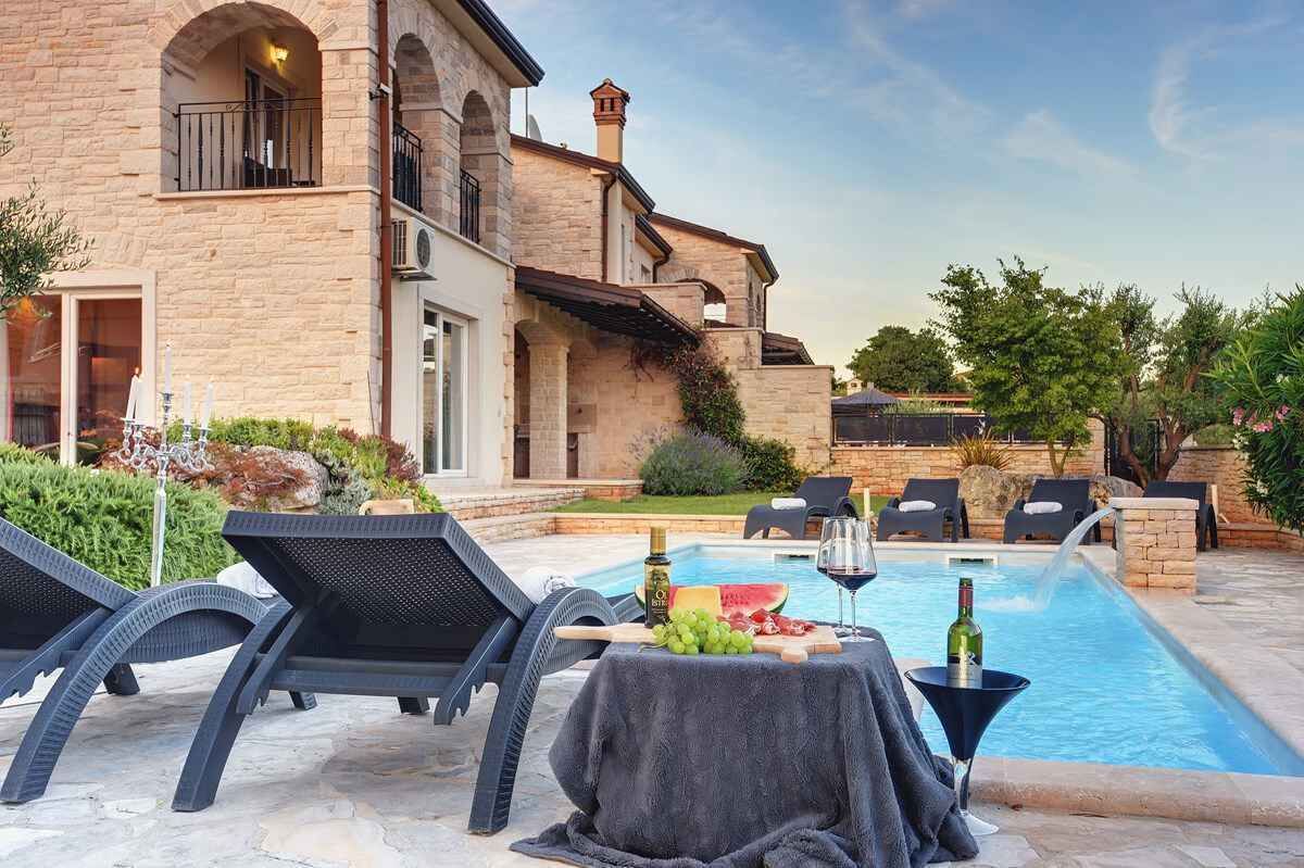 Área de piscina com espreguiçadeiras, uma mesa com uma garrafa de vinho e uma melancia.