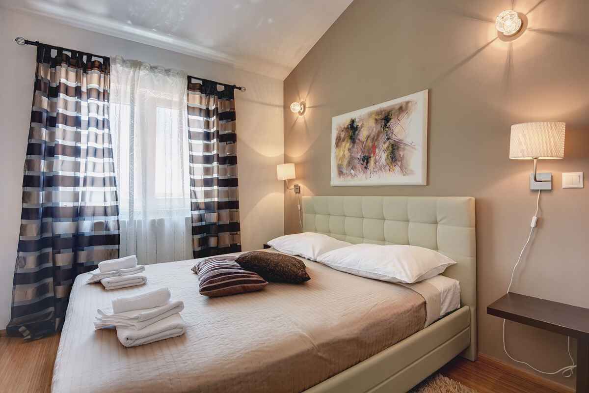 Ein ordentlich gemachtes Bett mit gefalteten Handtüchern, einem Kopfteil und einer Wandlampe.