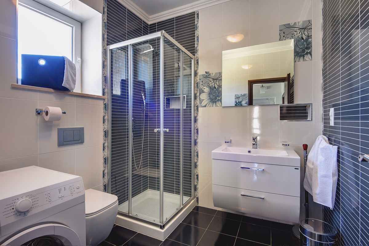 A modern bathroom with a glass-enclosed shower, a washing machine, a toilet, and a sink with a mirror.