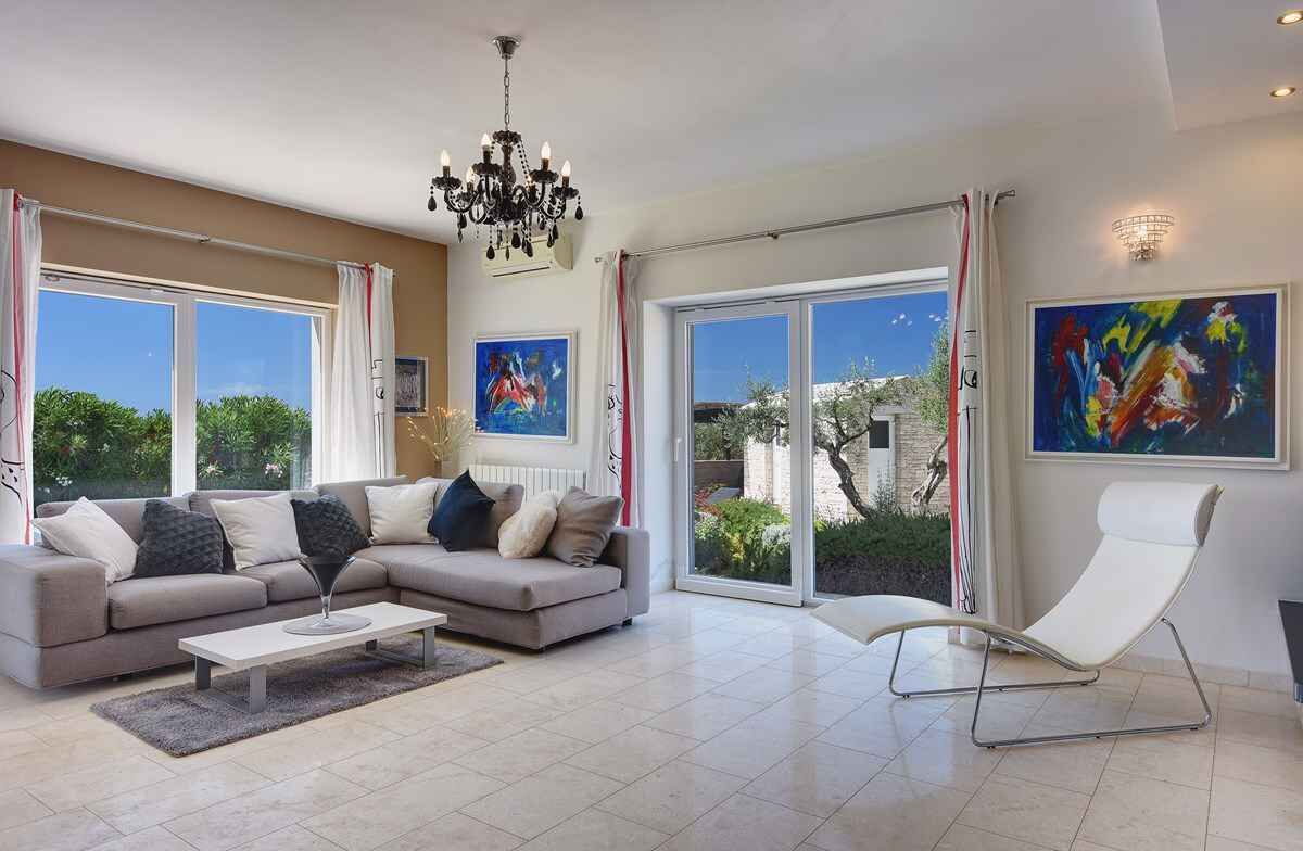 A modern living room with a sectional sofa, a coffee table, a white armchair, and large windows offering a view of greenery.