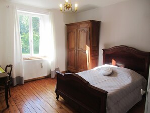 Un dormitorio con cama y armario de madera, un radiador, una ventana con cortinas y una silla.
