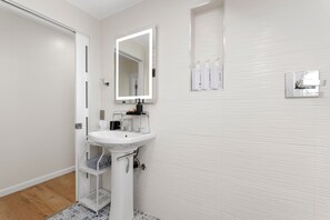 A bathroom with a white sink, mirror, and storage shelf. - Waikīkī Beach Loft Near Restaurants (Honolulu)