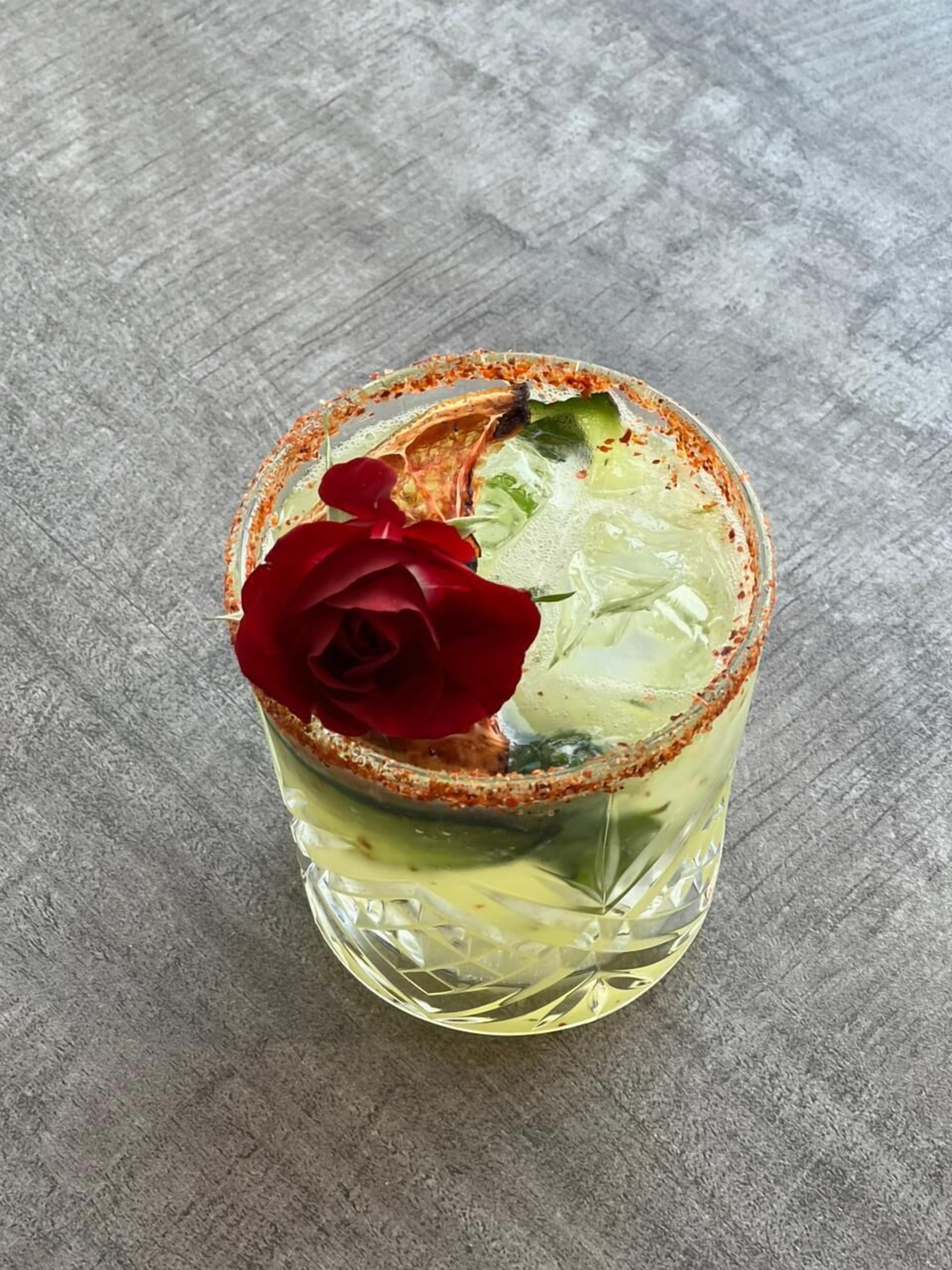 A glass with a salted rim and a red rose on a textured surface.