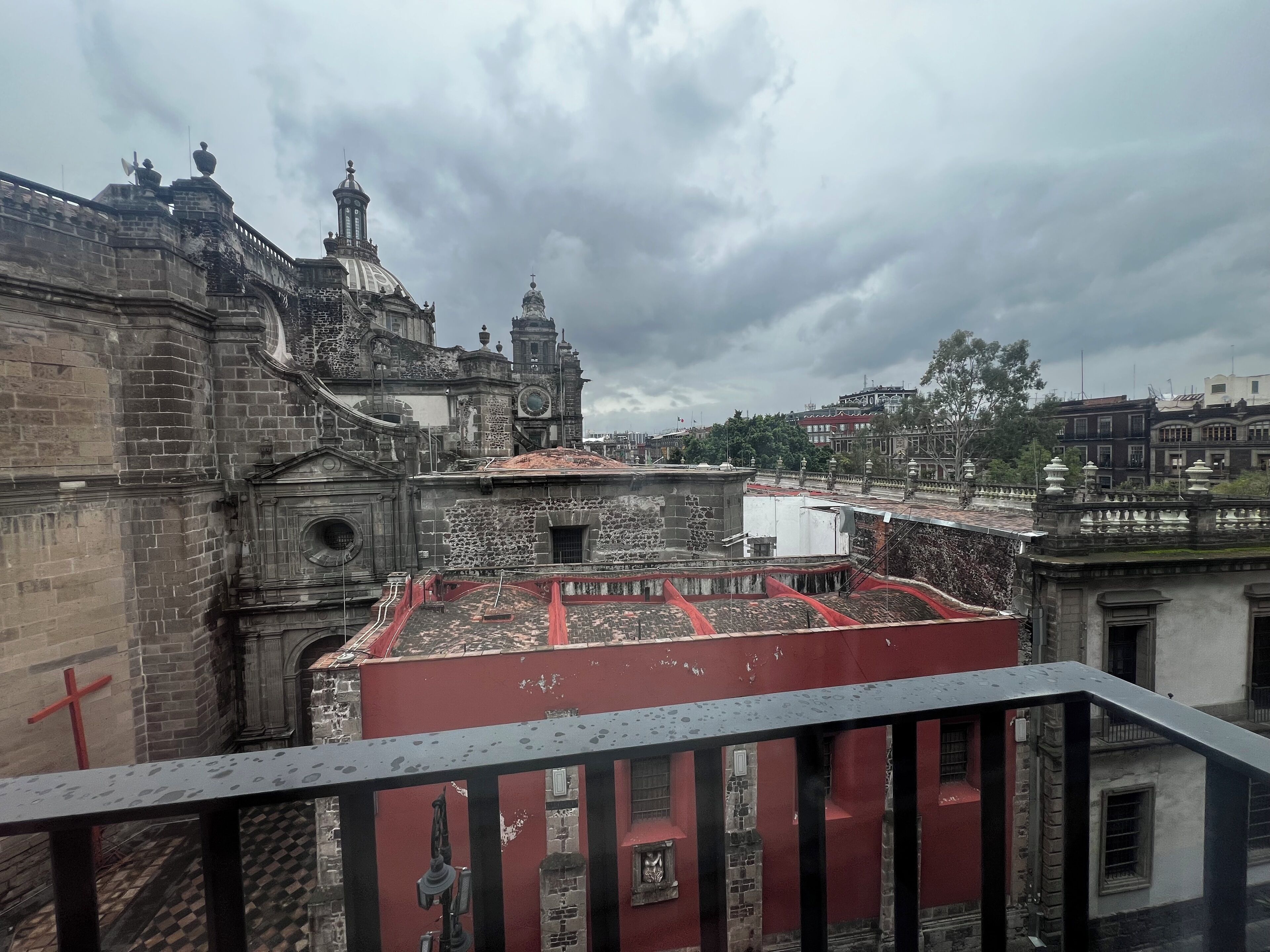 A historic building with a prominent dome and bell tower, featuring a red-roofed courtyard and a balcony with a metal railing.