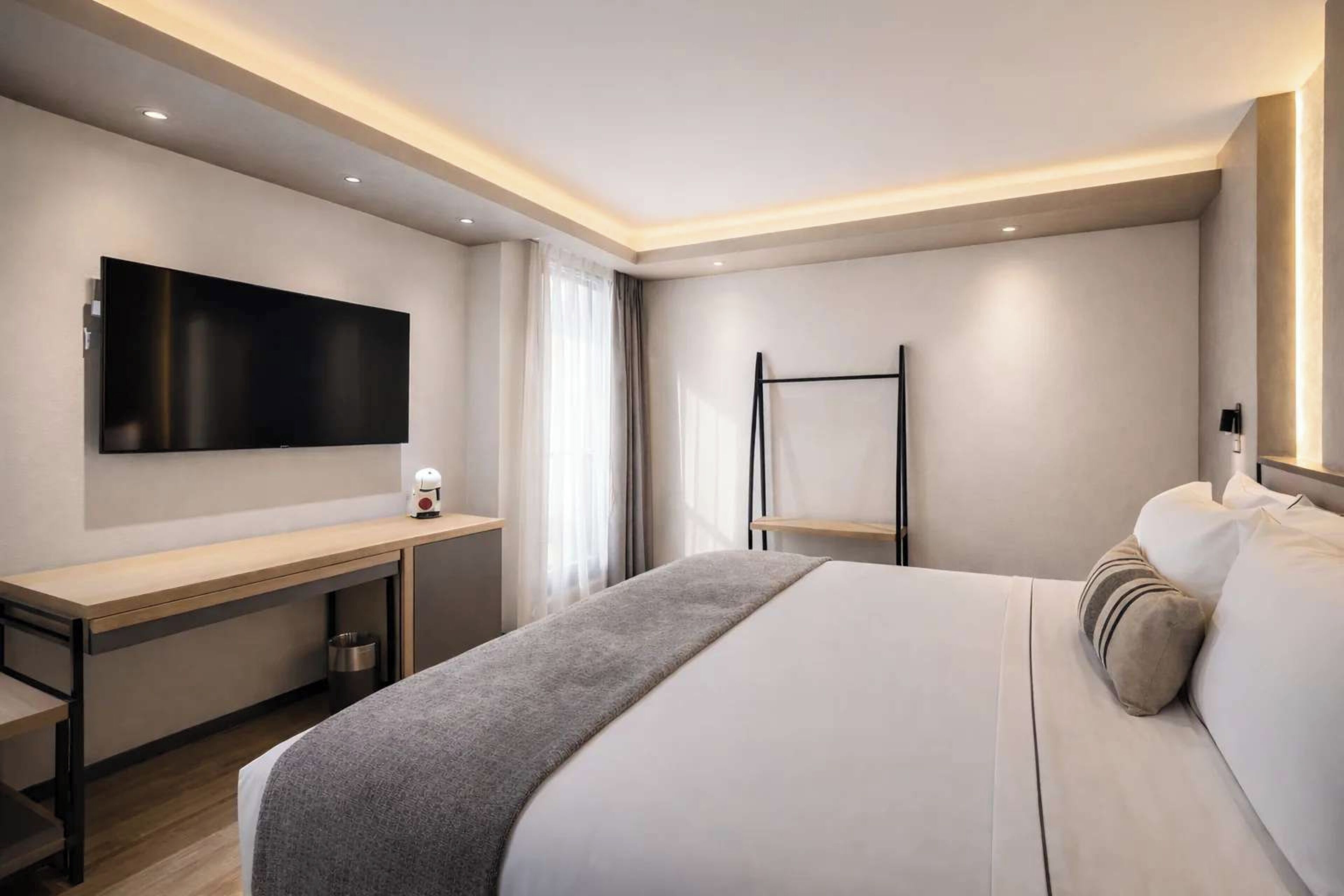 A modern hotel room with a bed, a desk, a flat-screen TV, and a bedside table.