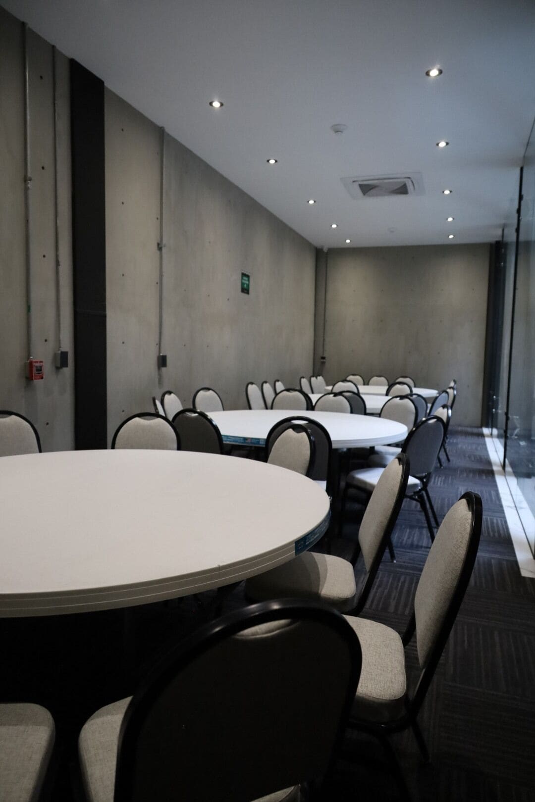A conference room with round tables and chairs, a plain wall, and a ceiling with recessed lighting.