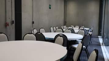 A conference room with round tables and chairs, a plain wall, and a ceiling with recessed lighting.