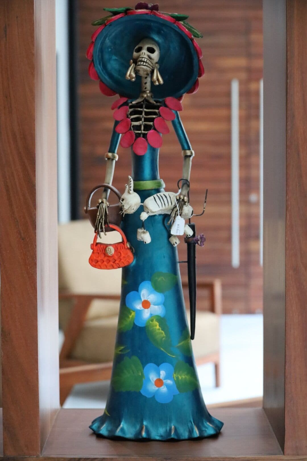 A decorative figure with a skull headpiece, a long skirt with floral patterns, and a red handbag.