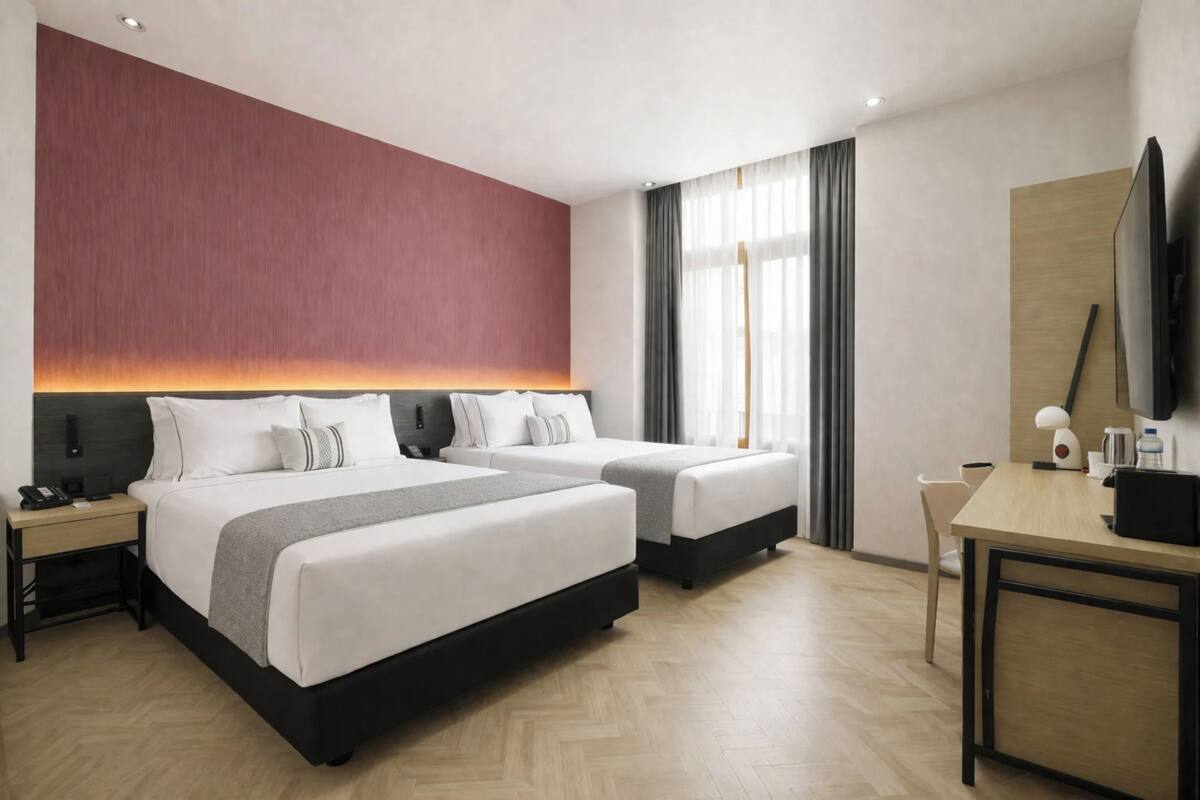 A hotel room with two beds, a desk, a chair, a TV, and a window with curtains.
