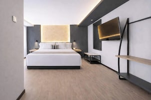 Une chambre d’hôtel moderne dotée d’un grand lit, de tables de chevet, d’un téléviseur à écran plat fixé au mur et d’un design minimaliste.