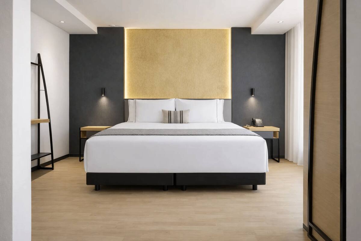 A modern hotel room with a large bed, bedside tables, and a wall-mounted light fixture.