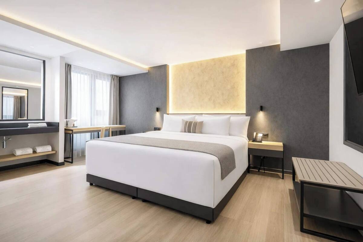 A modern hotel room with a large bed, bedside tables, a desk, and a mirror.