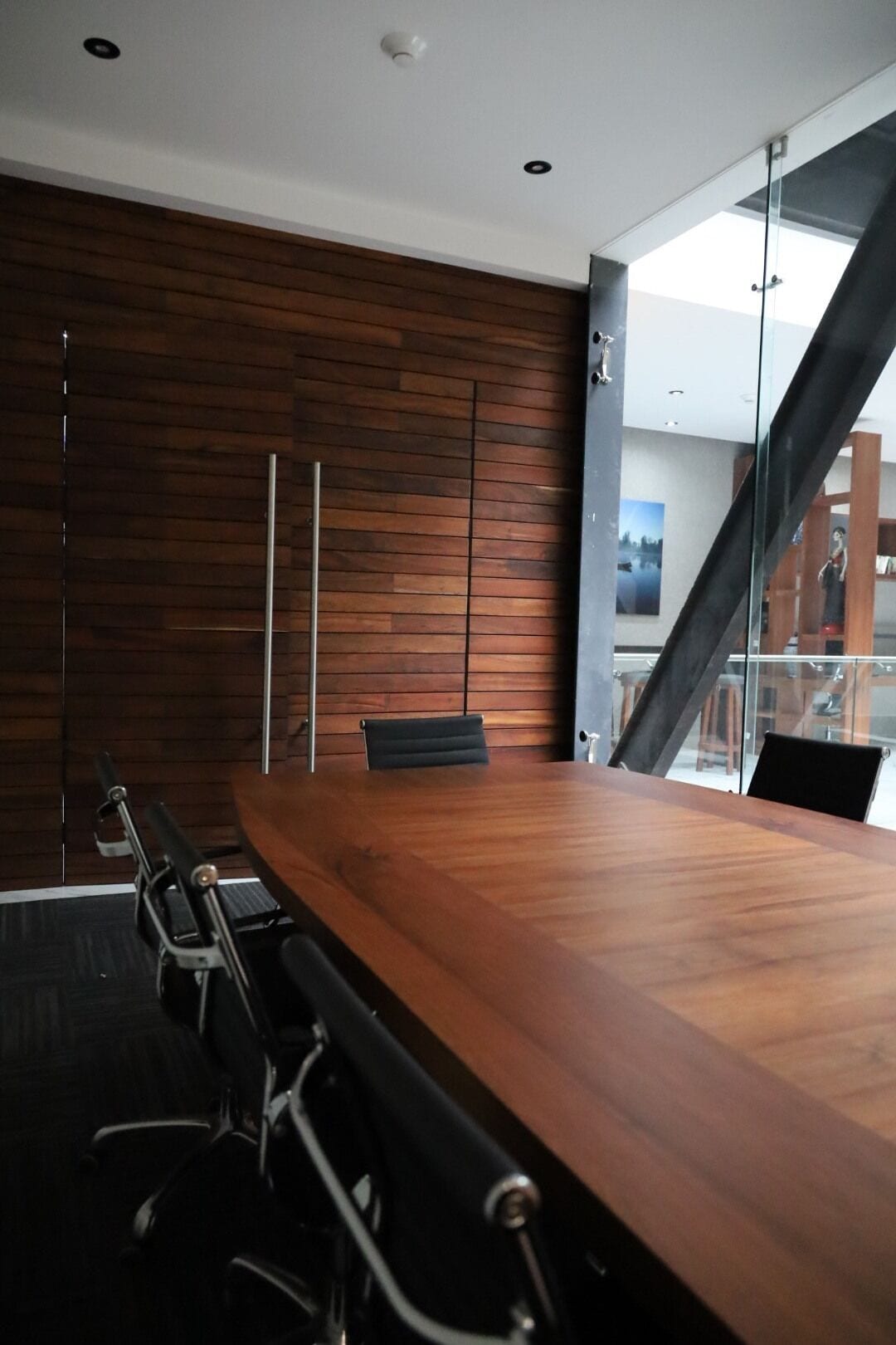 Ein Konferenzraum mit einem Holztisch, schwarzen Stühlen und einer Glastrennwand.