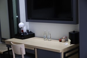 A hotel room with a desk, two bottles of water, a lamp, a black trash bin, and a TV. - Hotel Catedral (Mexico City)
