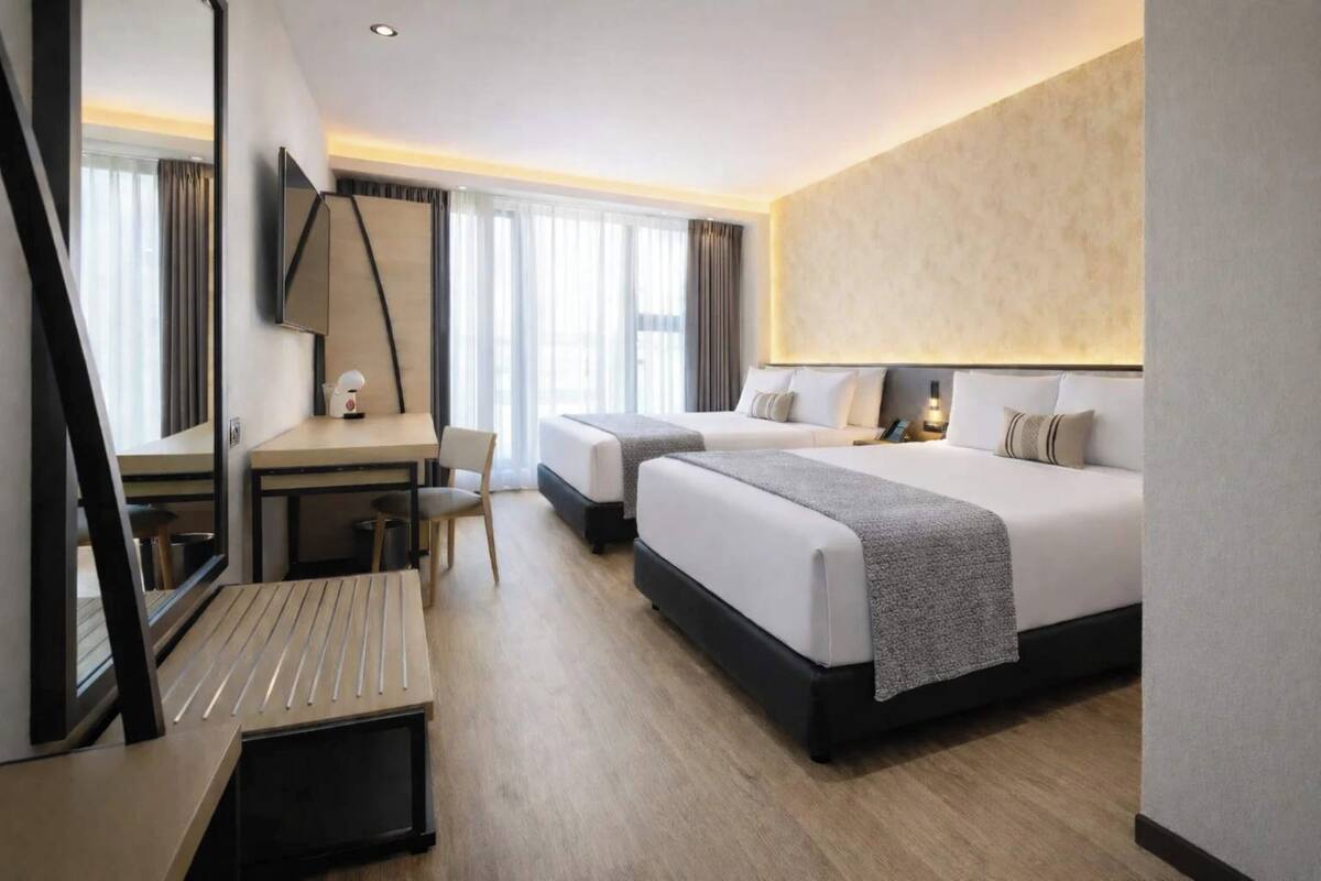 A hotel room with two beds, a desk, a chair, and a large mirror.