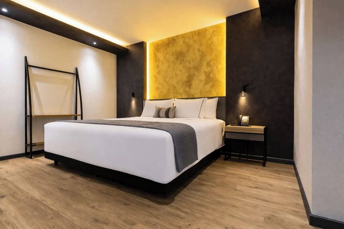 A modern bedroom with a large bed, bedside tables, and a headboard with built-in lighting.