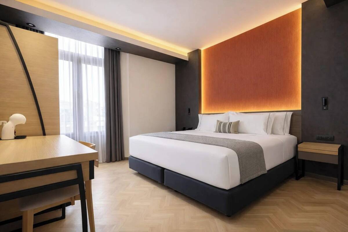 A modern hotel room with a large bed, a desk, and a view of the outdoors.