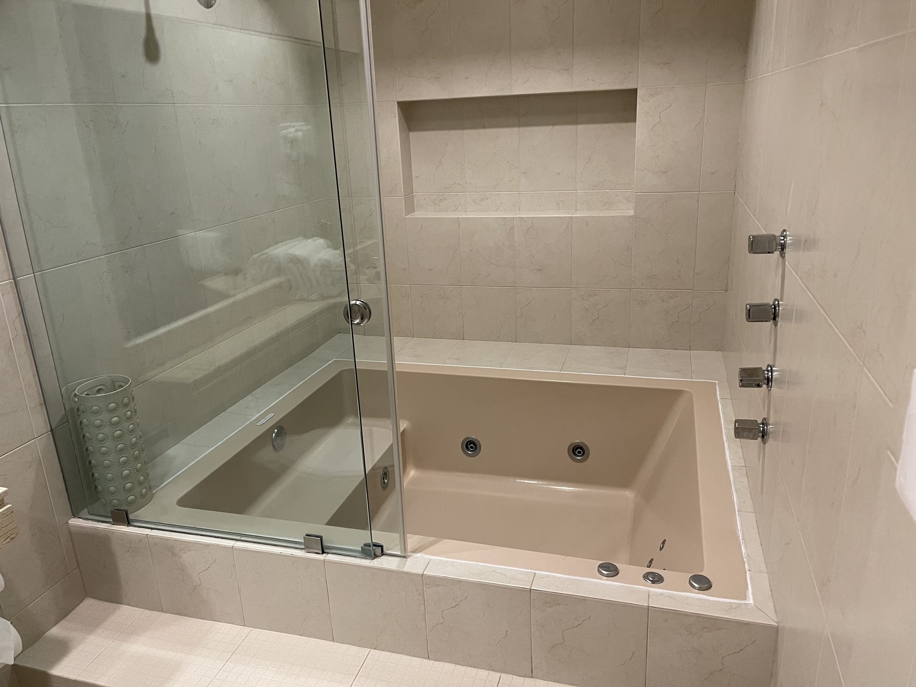 Un baño moderno con ducha de vidrio, bañera integrada y un pequeño estante.