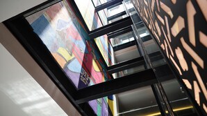 Um interior moderno com teto de vidro, padrões geométricos nas paredes e uma escadaria.