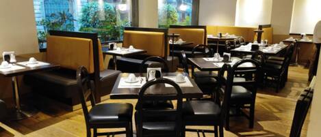 Un restaurante con cabinas y mesas, piso de madera y amplias ventanas con vistas a edificios y zonas verdes.