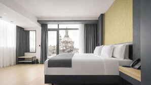 Quarto de hotel moderno com uma cama grande, escrivaninha e vista para a cidade.