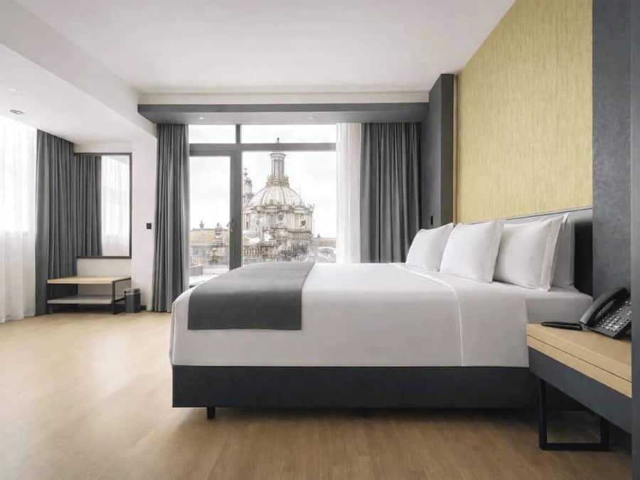 A modern hotel room with a large bed, a desk, and a city view.