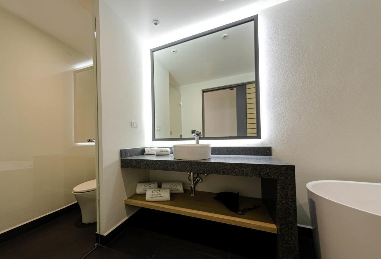 Un baño moderno con un lavamanos blanco, un espejo grande y un perchero para toallas.