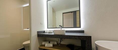 Un baño moderno con un lavamanos blanco, un espejo grande y un perchero para toallas.