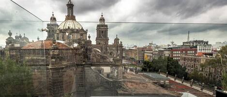 A view from a high balcony with a glass barrier, overlooking a historic building with domes and towers, and a cityscape in the background.