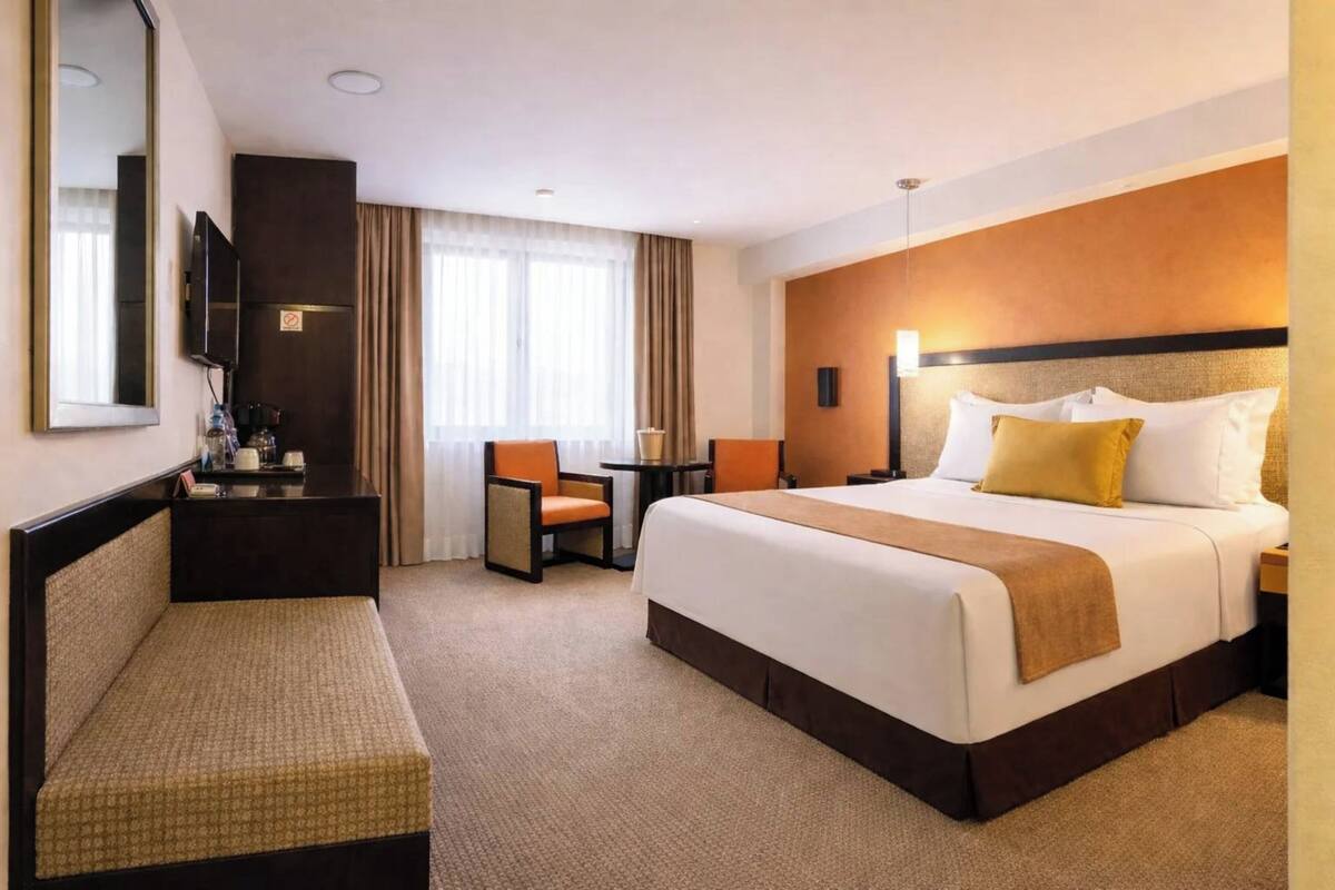 A hotel room with a large bed, a desk, a chair, and a small table.