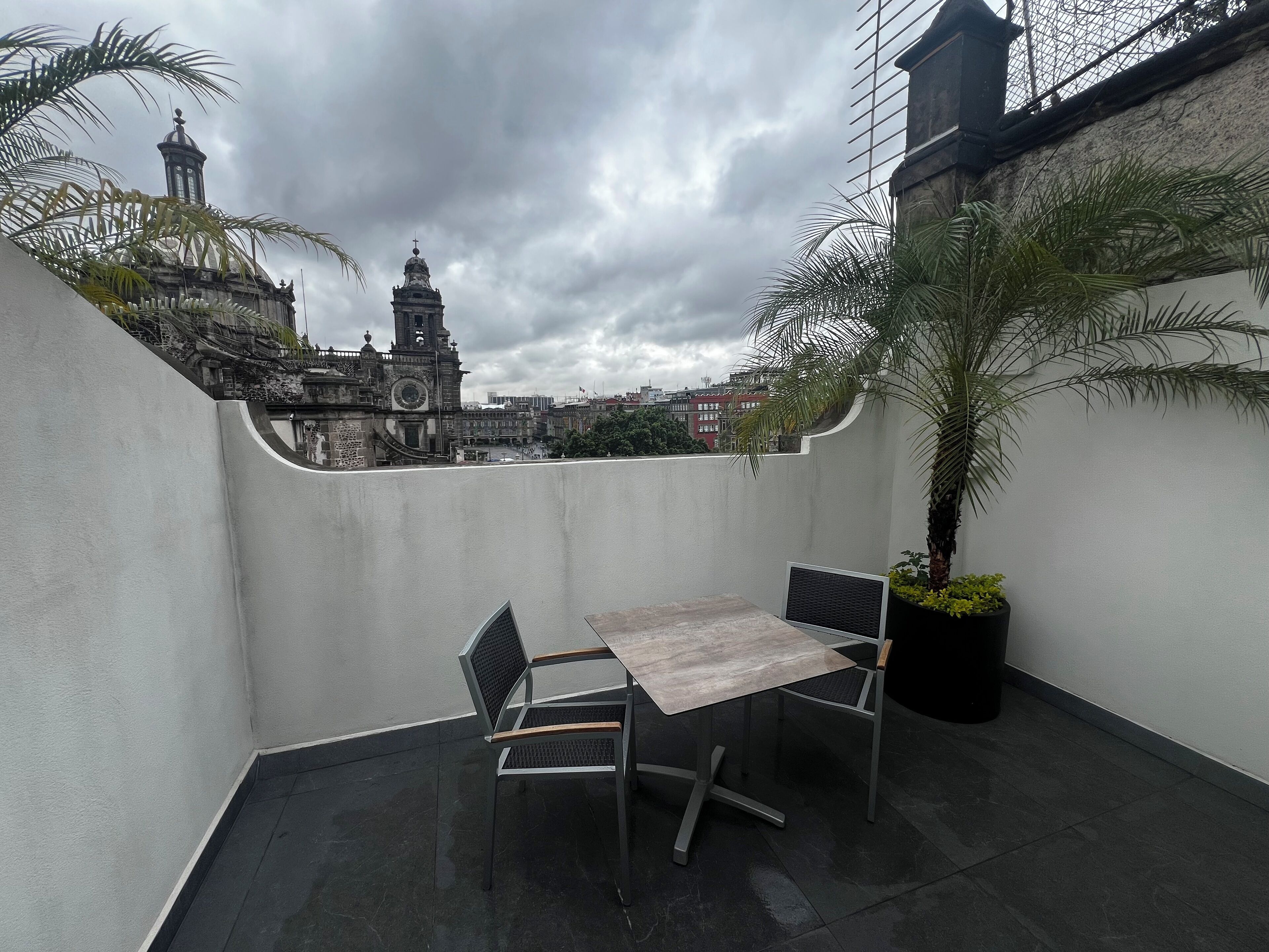 A rooftop terrace with a table and chairs, a potted plant, and a view of a historic building with a clock tower.