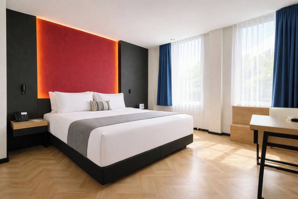 A modern hotel room with a large bed, bedside tables, a desk, and a view of the outdoors.