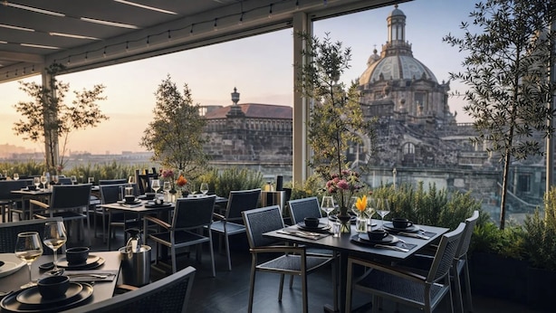 Restaurante com mesas preparadas para refeições, vista para um edifício histórico e plantas em vasos.