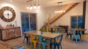 Un vaste espace dédié à la salle à manger, avec une table en bois et des chaises colorées, une grande horloge murale et un escalier menant à un niveau supérieur.