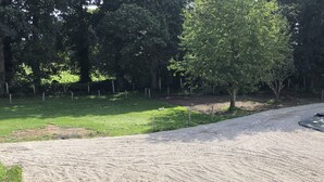 Une allée de gravier mène à une zoneClose délimitée par une clôture, où se trouvent des arbres et de l’herbe.