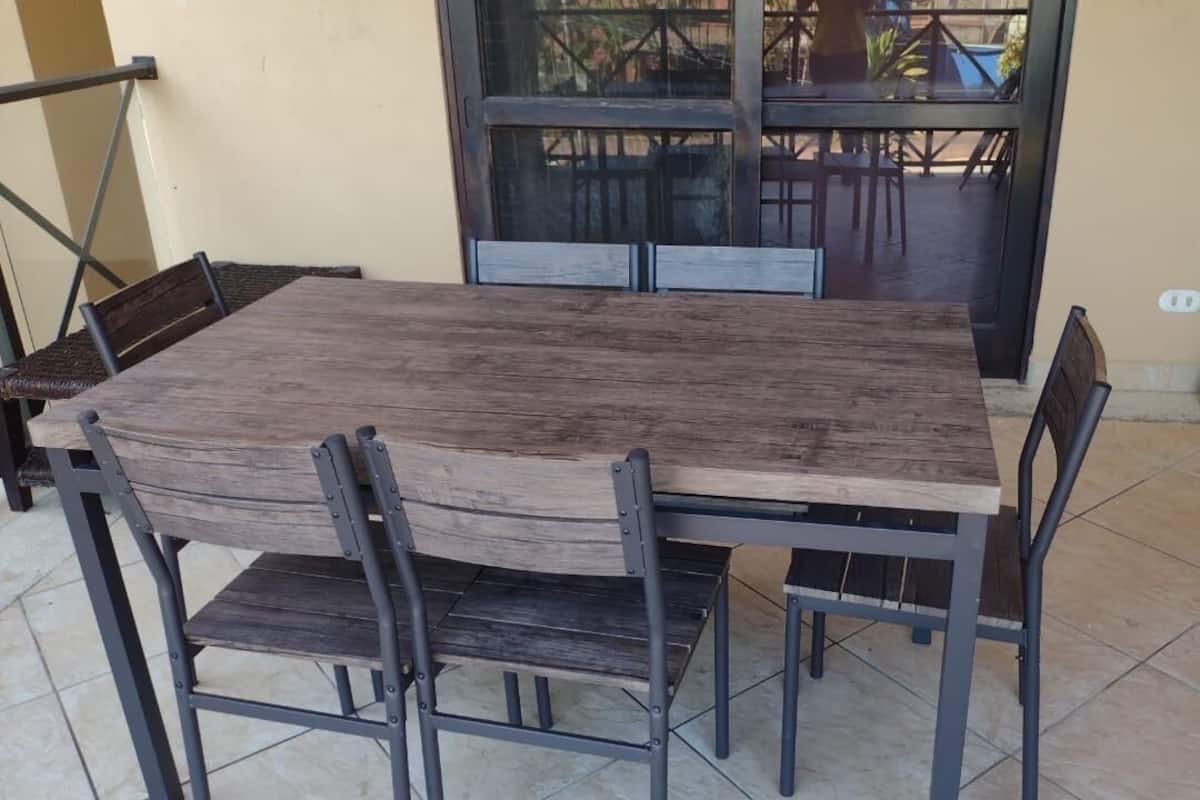Une table rectangulaire en bois, entourée de chaises en métal, posée sur un sol carrelé.