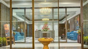 Un vestíbulo con separador de vidrio, sofás azules, una mesa central con arreglo floral y un candelabro.