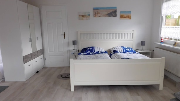 A bedroom with a bed, a wardrobe, a nightstand, and a window with a view of the beach. - Lovingly furnished holiday home in a quiet location (Ellenberg)