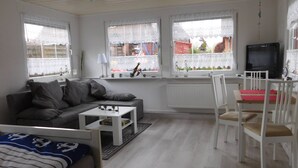 A living room with a grey sofa, a white coffee table, a TV, and a dining area with white chairs. - Lovingly furnished holiday home in a quiet location (Ellenberg)