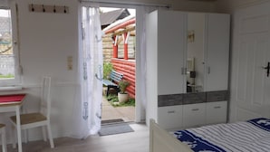 A bedroom with a bed, a desk, and a wardrobe. There is a door leading to an outdoor area with a bench and a red structure. - Lovingly furnished holiday home in a quiet location (Ellenberg)