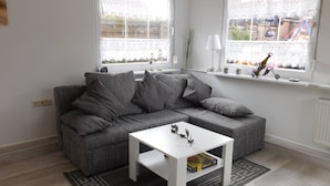 A modern living room with a grey sofa, a white coffee table, and two windows with lace curtains. - Lovingly furnished holiday home in a quiet location (Ellenberg)