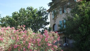 Un bâtiment doté d’un balcon, entouré d’arbres et de plantes fleuries.