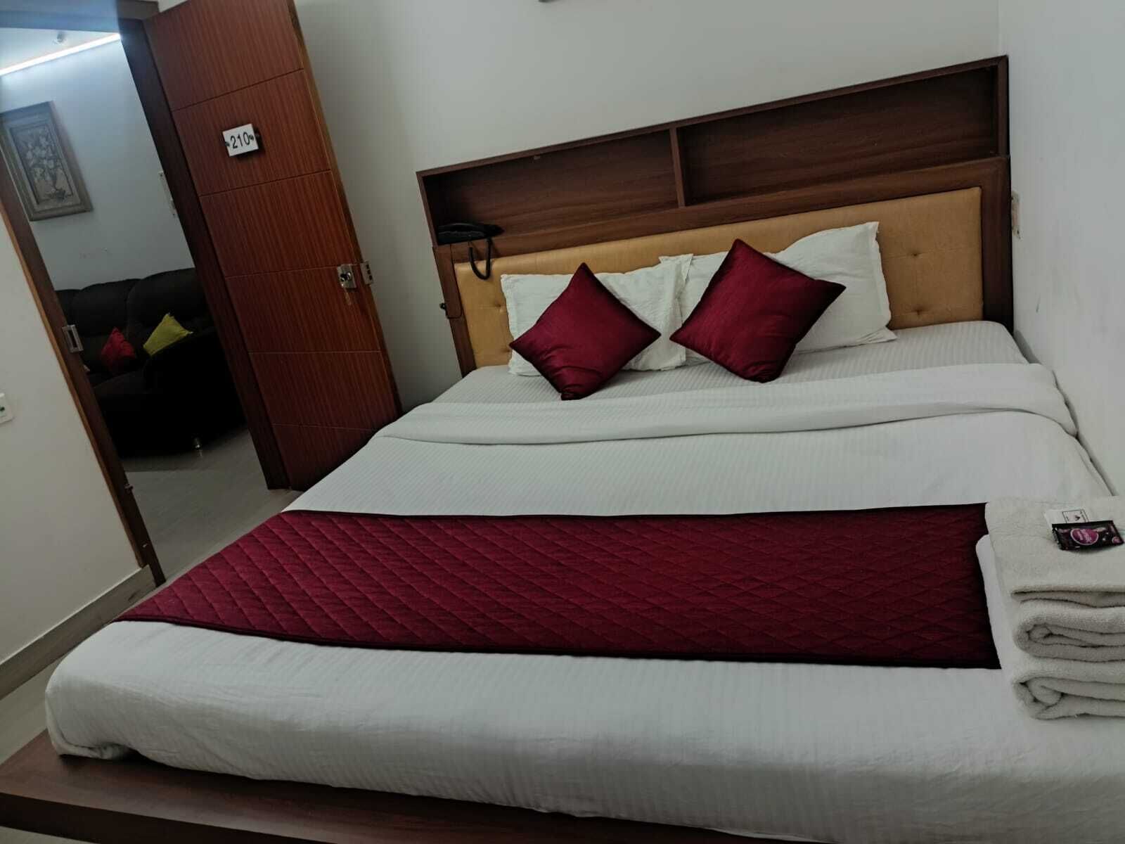 A neatly made bed with white and red bedding, a wooden headboard, and a red quilted blanket.