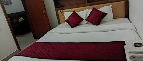 A neatly made bed with white and red bedding, a wooden headboard, and a red quilted blanket.