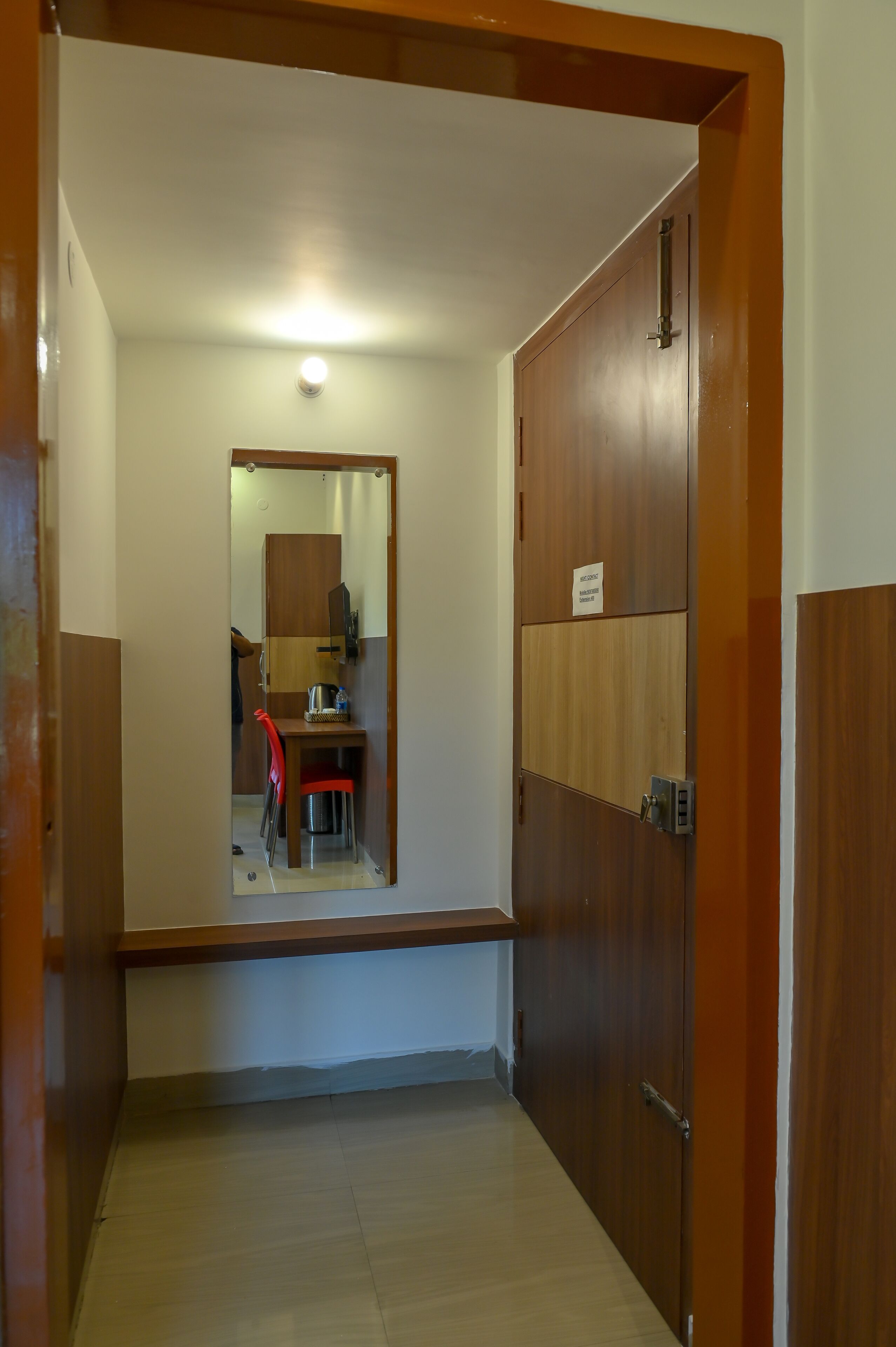 Un pasillo con una puerta de madera, una mesa pequeña con una silla y un espejo en la pared.