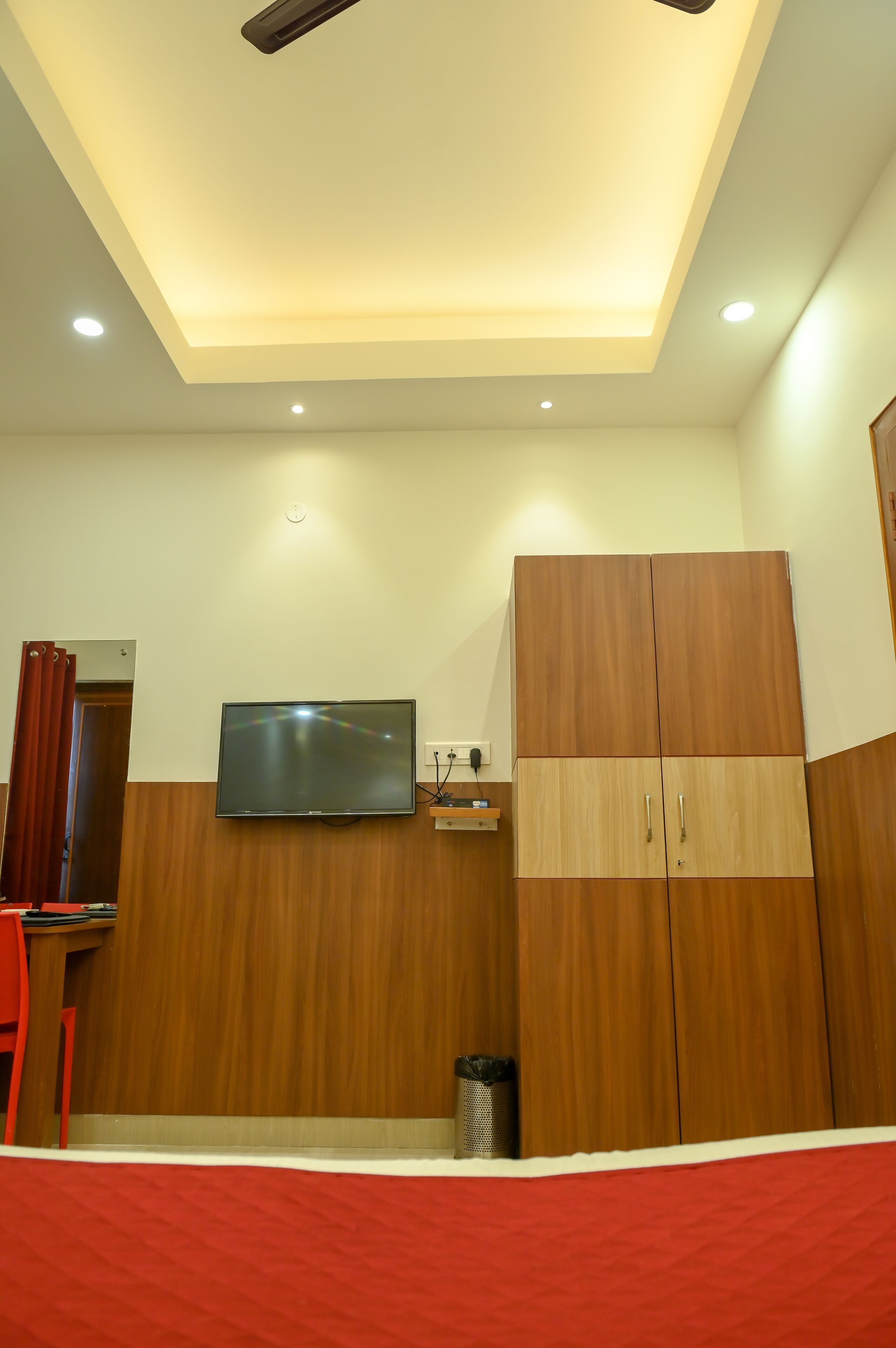 Une pièce dotée d’un ventilateur de plafond, d’un éclairage encastré, d’un téléviseur à écran plat fixé au mur, d’une armoire en bois et d’un lit rouge.
