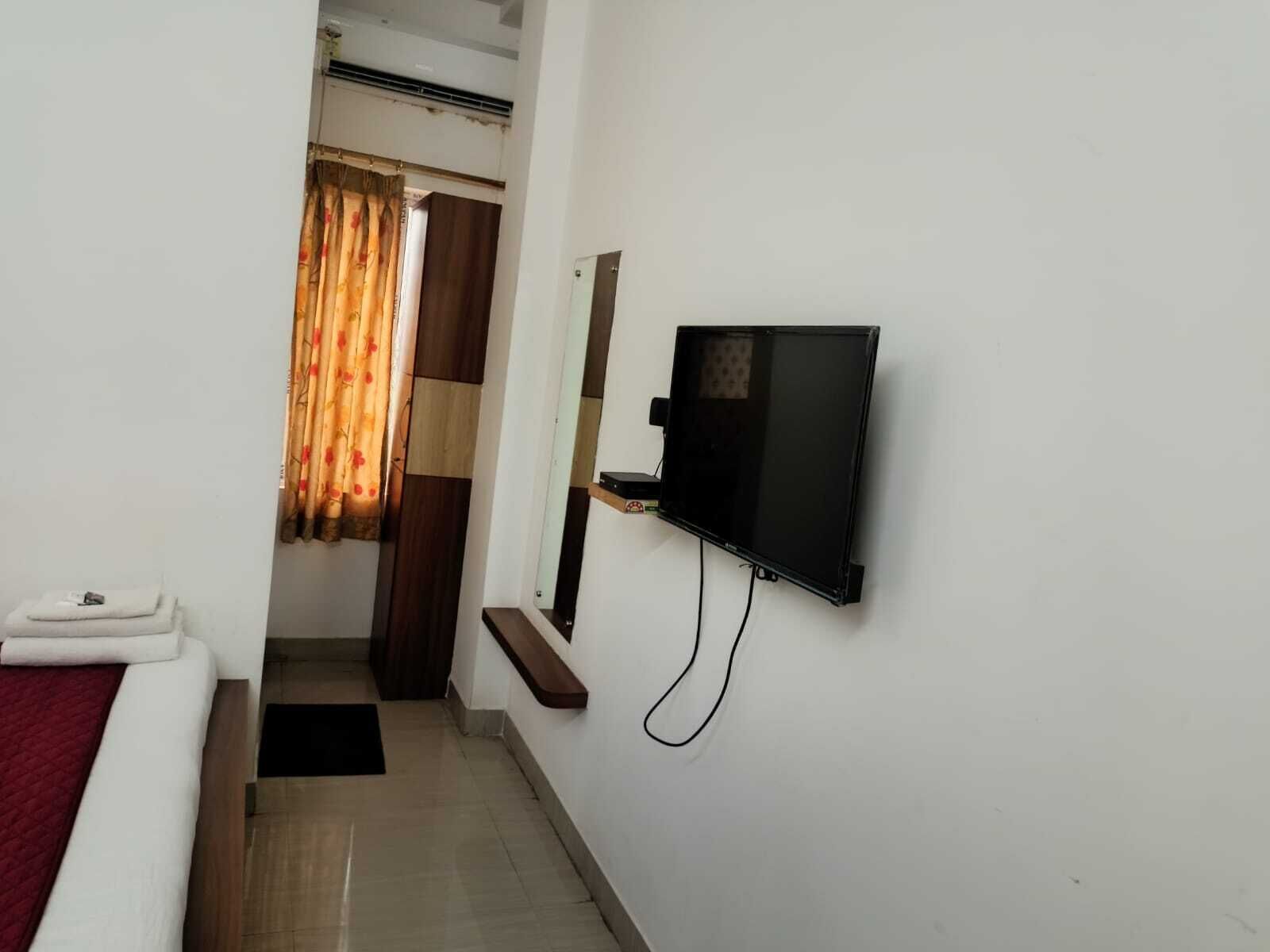 Una camera d'albergo con un letto, una TV a muro, un piccolo ripiano e una porta con tende.