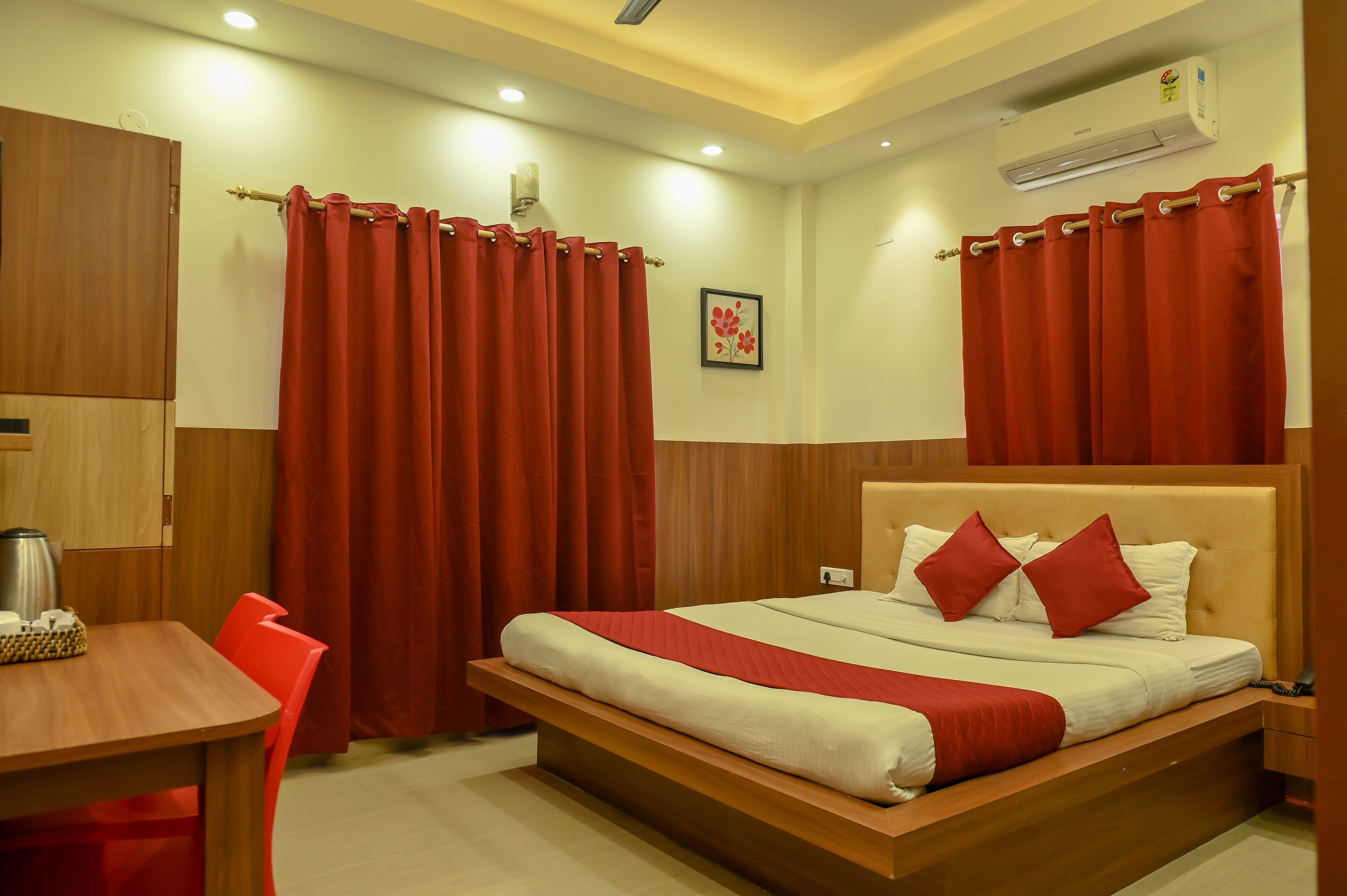 A hotel room with a wooden bed, red curtains, a wooden desk, and a coffee pot.